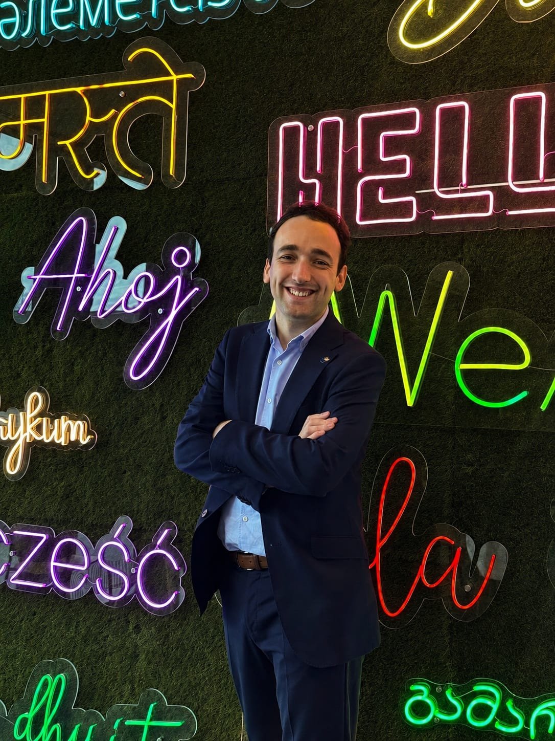 Aitor Ugarte, en traje, ante un muro de saludos de neón en varios idiomas